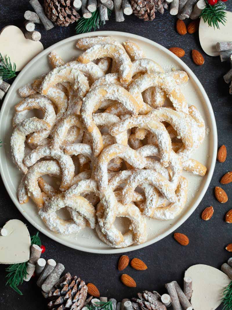 Almond crescent cookies covered in white powder sugar serve on a white round plate