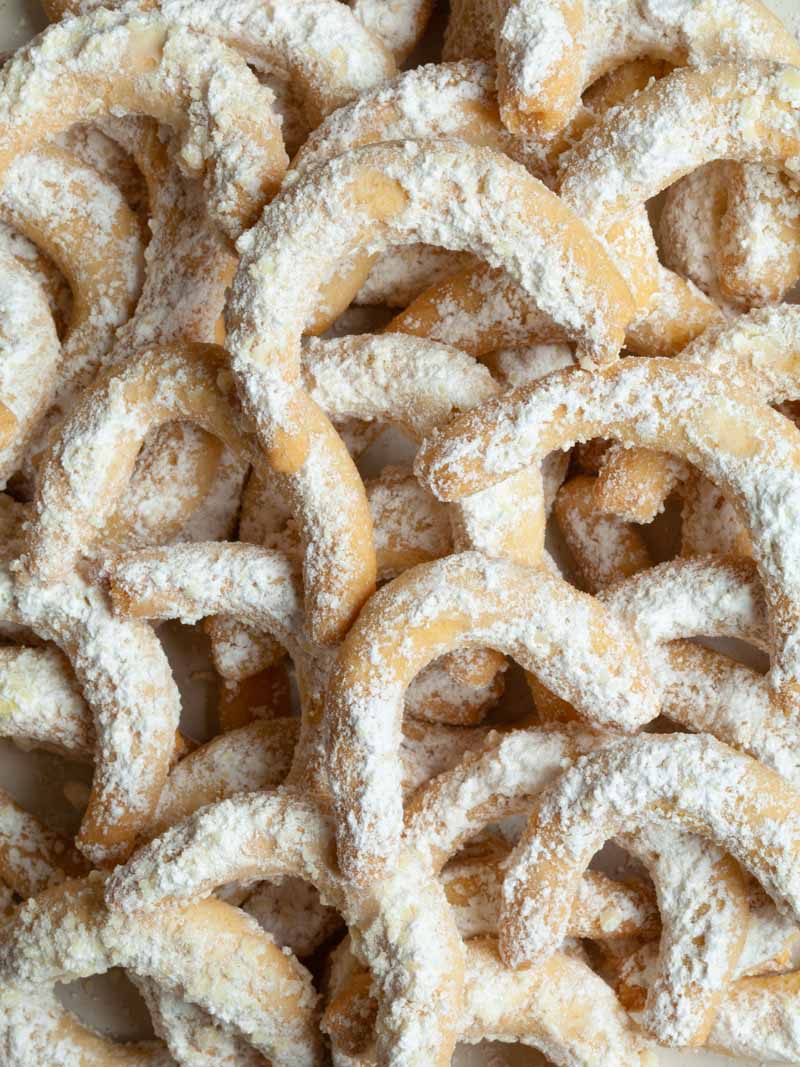 A very close photo of a light brown almond crescent cookies covered in white icing sugar.
